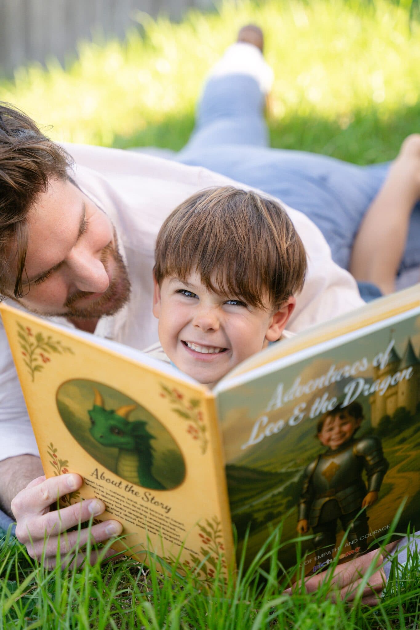 A boy grinning over the top of Adventures of Leo & the Dragon while his dad reads it to him