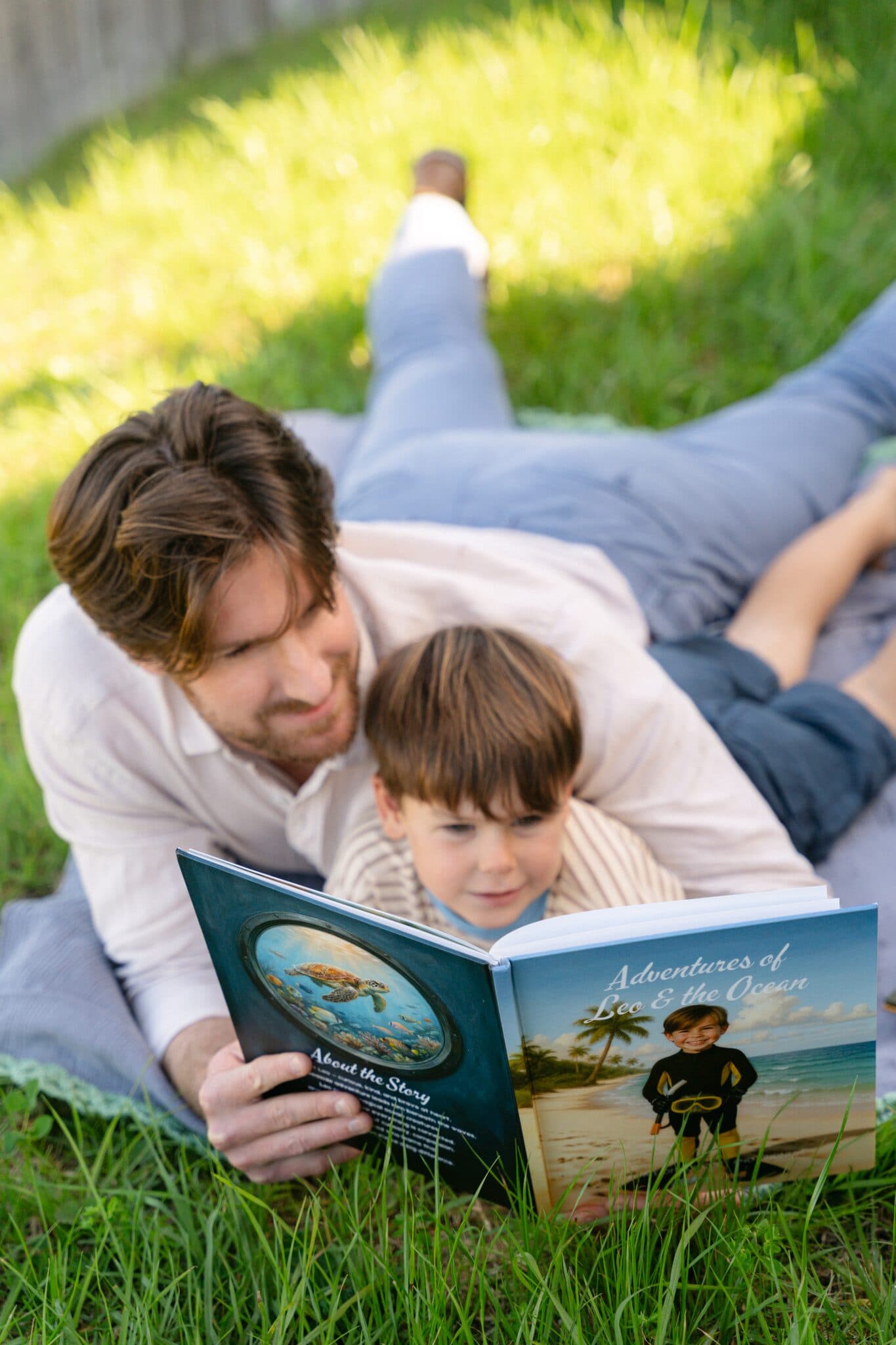 A dad and his son reading the ocean story together on the grass