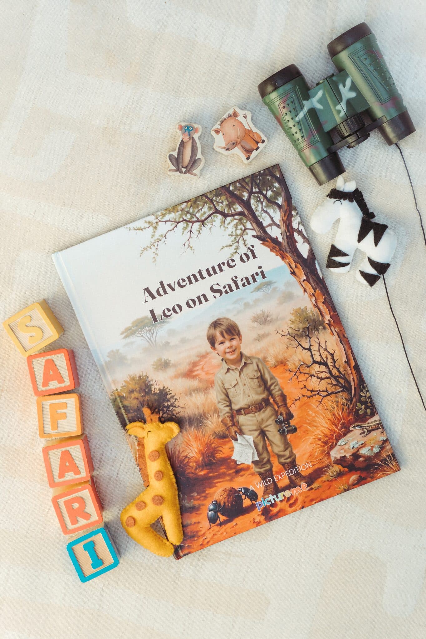 The safari hardcover laid out with binoculars, a toy giraffe and letter blocks spelling SAFARI