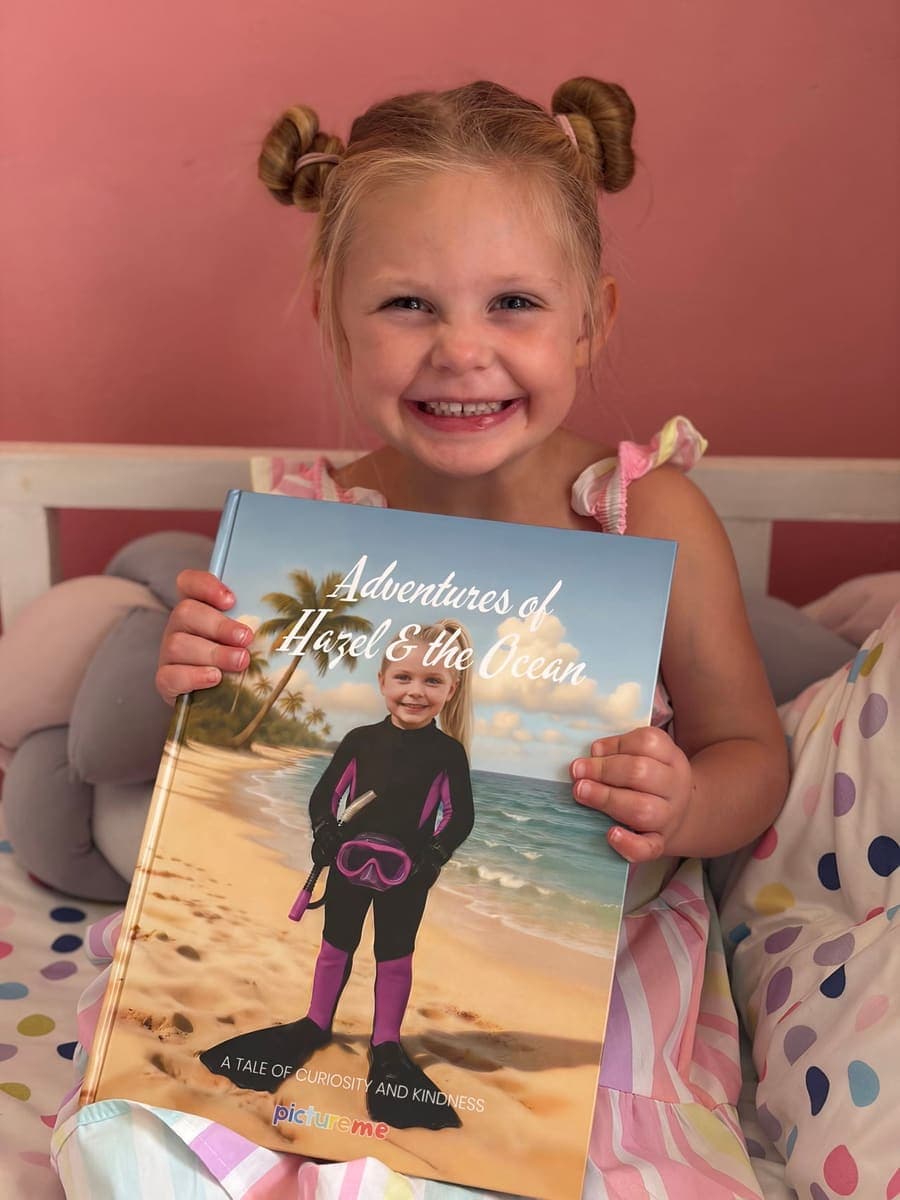 A little girl beaming as she holds up her personalised Adventures of Hazel & the Ocean book