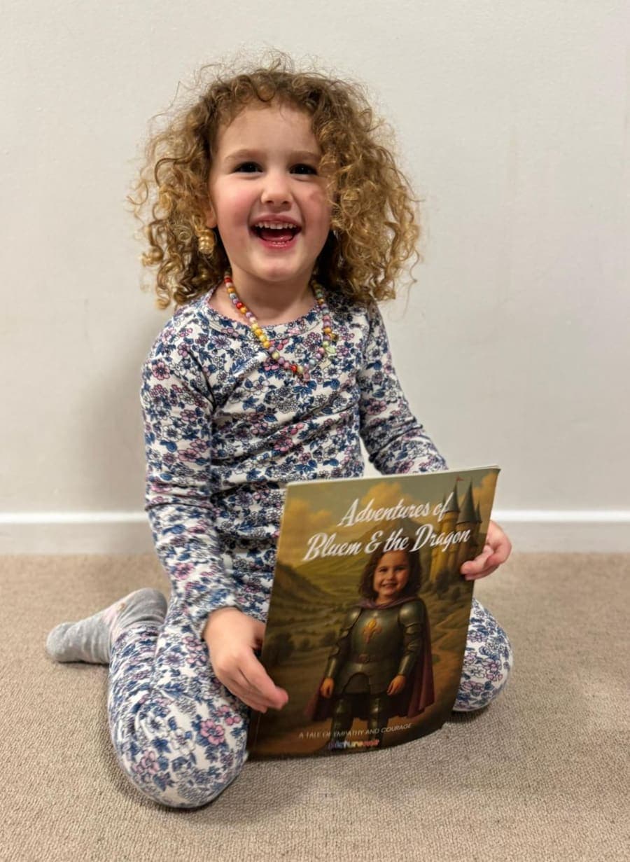 A laughing girl in pyjamas holding her personalised Adventures of Bluem & the Dragon book