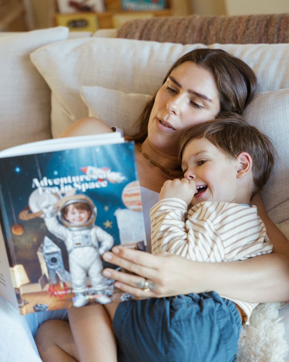 The same boy giggling on the couch with his mother, his astronaut likeness on the space book's cover