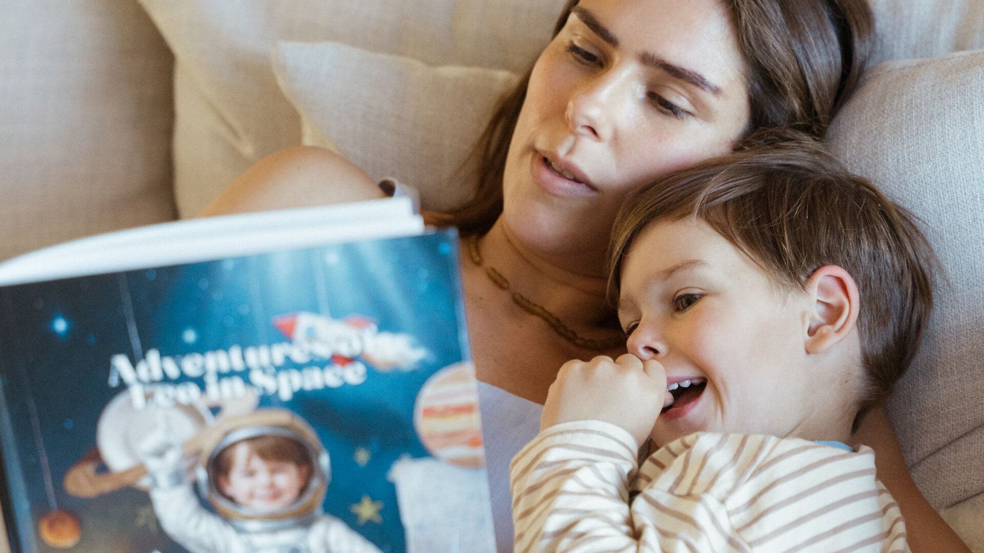 The same boy giggling on the couch with his mother, his astronaut likeness on the space book's cover