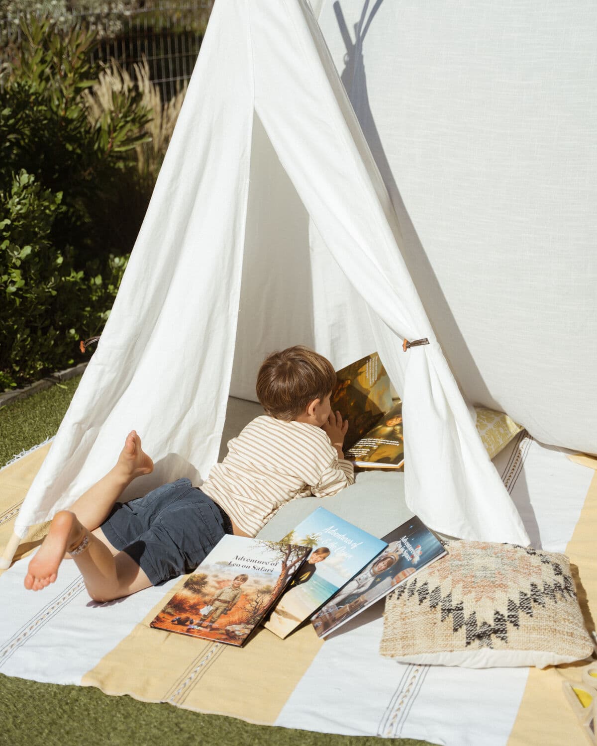 The boy lying in his play tent reading, with his safari, ocean and space books scattered on the blanket