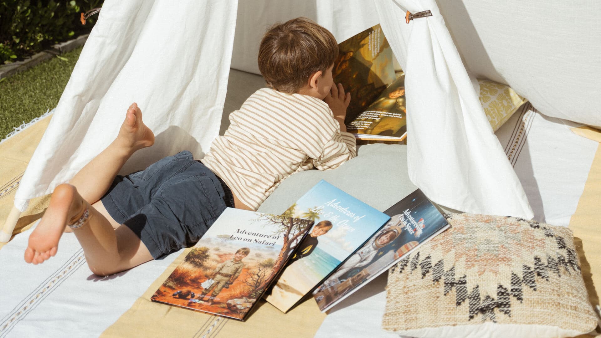 The boy lying in his play tent reading, with his safari, ocean and space books scattered on the blanket