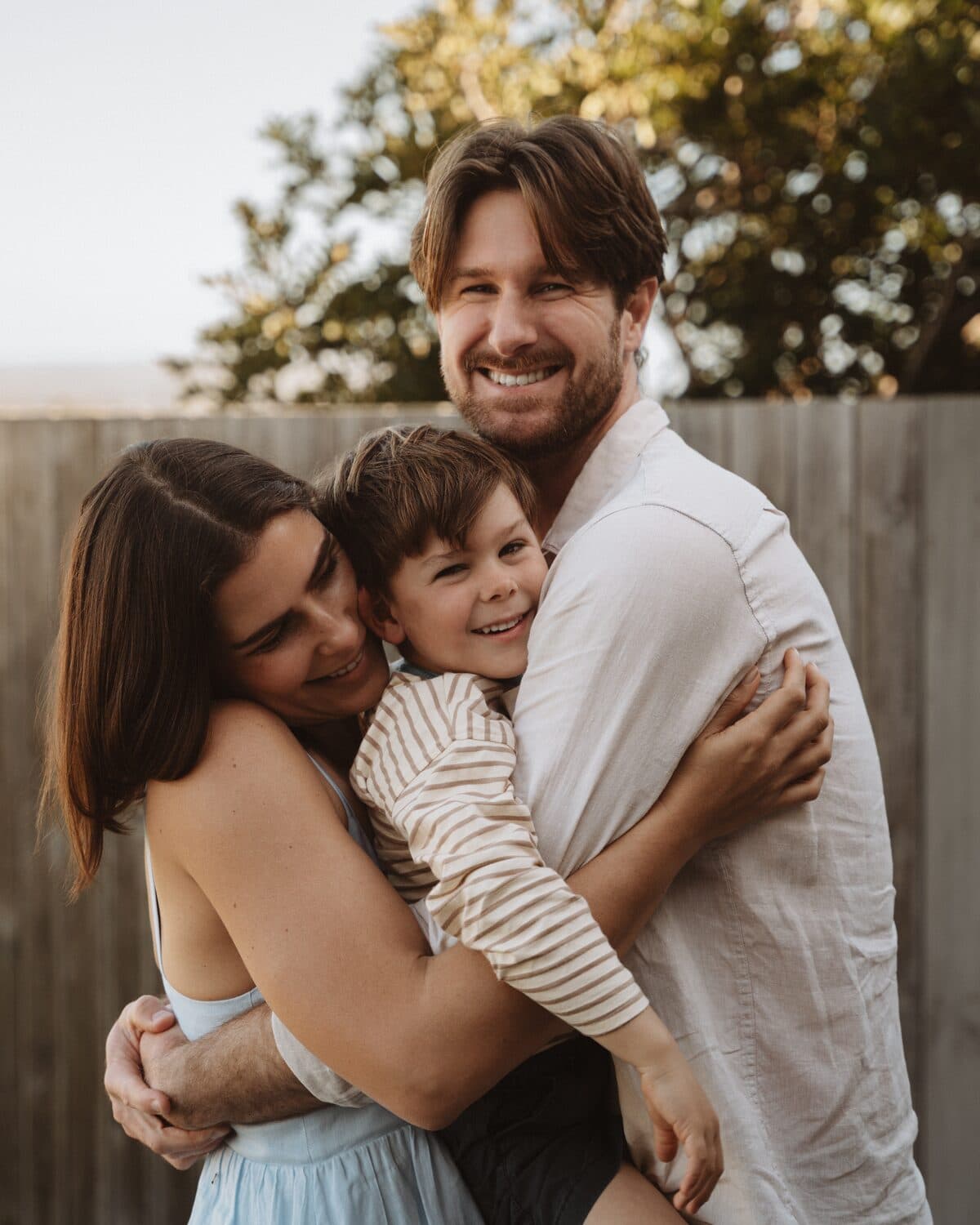 Nick, Michaella and their son in a family hug at golden hour